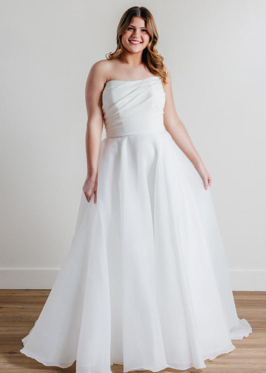 Introducing Fortune, the epitome of elegance and sophistication in bridal fashion. This exquisite wedding dress boasts a timeless strapless design, crafted with meticulous attention to detail. Its luxurious blend of Cyrus Stretch Crepe and Sluler Satin Organza fabrics creates a breathtaking A-line silhouette that will make any bride feel like a true vision of romance on her special day. 