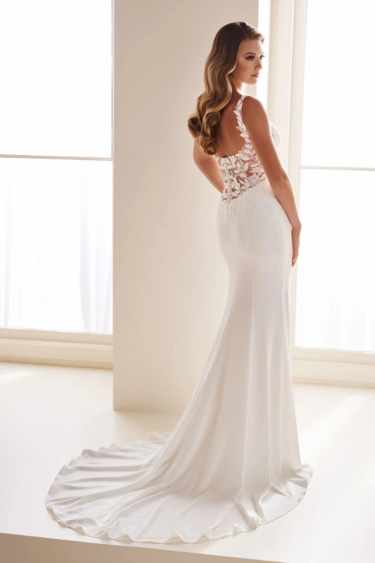 A woman modeling a white bridal gown from the back in a bright, minimalist indoor setting with large windows and white walls.