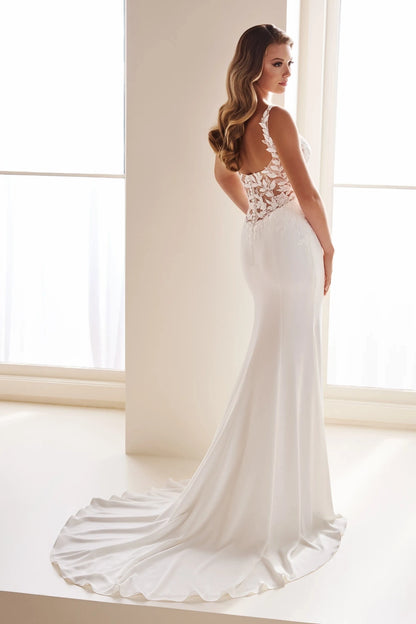 A woman modeling a white bridal gown from the back in a bright, minimalist indoor setting with large windows and white walls.