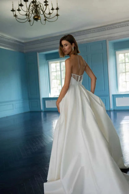 The Mollie gown adds thoughtful details to a classic silhouette. Featuring a beautifully structured bodice with a sultry scoop neckline with high peaks, the full A line skirt is elevated by inverted box pleats and a dramatic side slit. The sheer illusion back with exposed boning ensures a beautiful view from any angle, and covered buttons to the hem add one last classic bridal detail.