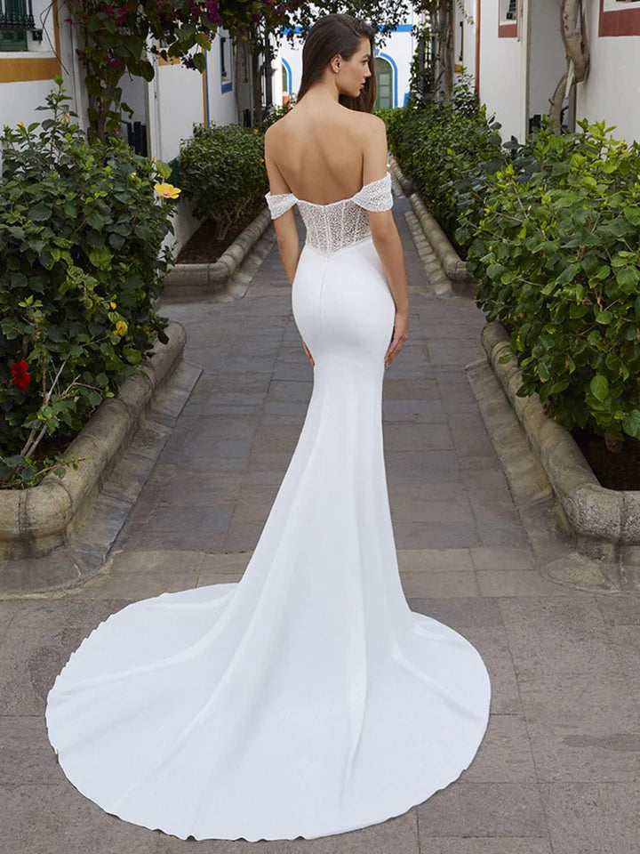 Woman in a white mermaid-style wedding dress with a long train on a paved path.