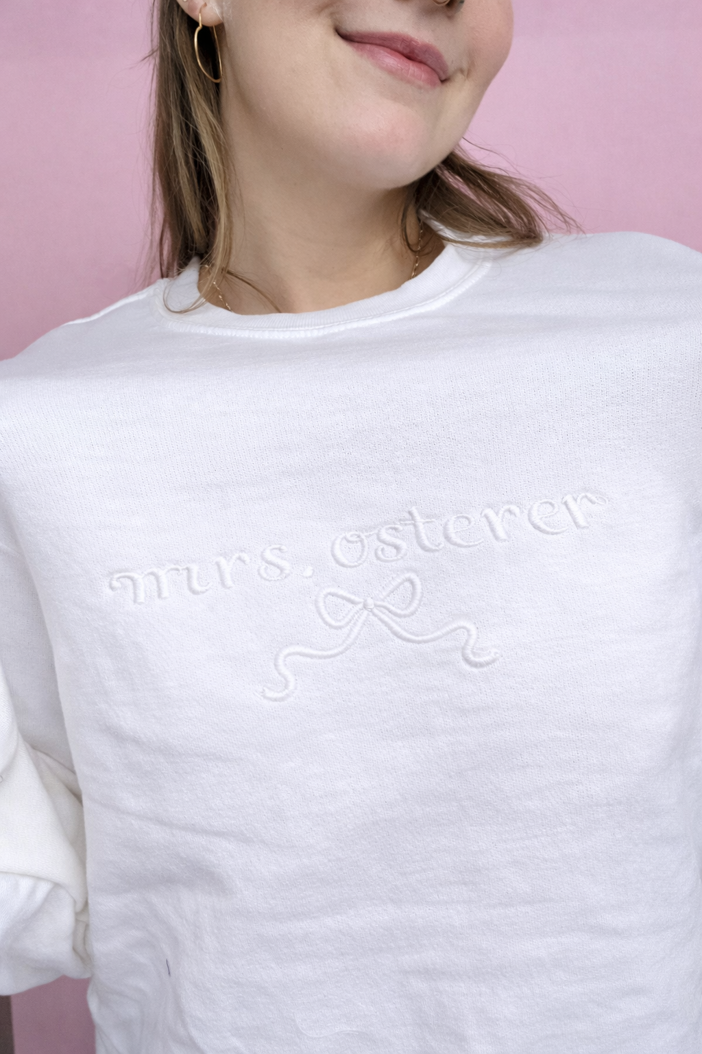 White sweatshirt with personalized "mrs" embroidered text worn by Abby against a pink background