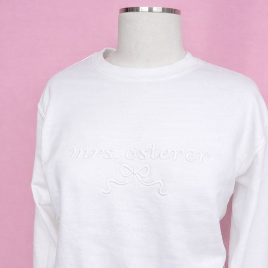 White unisex crewneck sweatshirt with mrs last name on a mannequin against a pink background