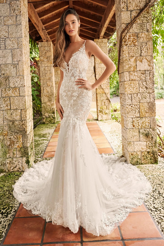 A woman models a white lace mermaid-style wedding gown under a stone colonnade with terracotta tile flooring and greenery in the background. JESSA by Martin Thornburg at NKIN
