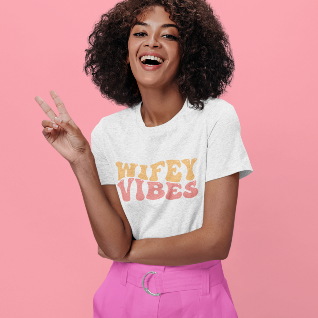 A young woman wearing a white t shirt with "wifey vibes" written in pastel retro colors.