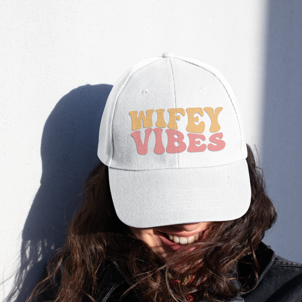 a young woman wearing a white hat that says "wifey vibes" in retro pastel writing.