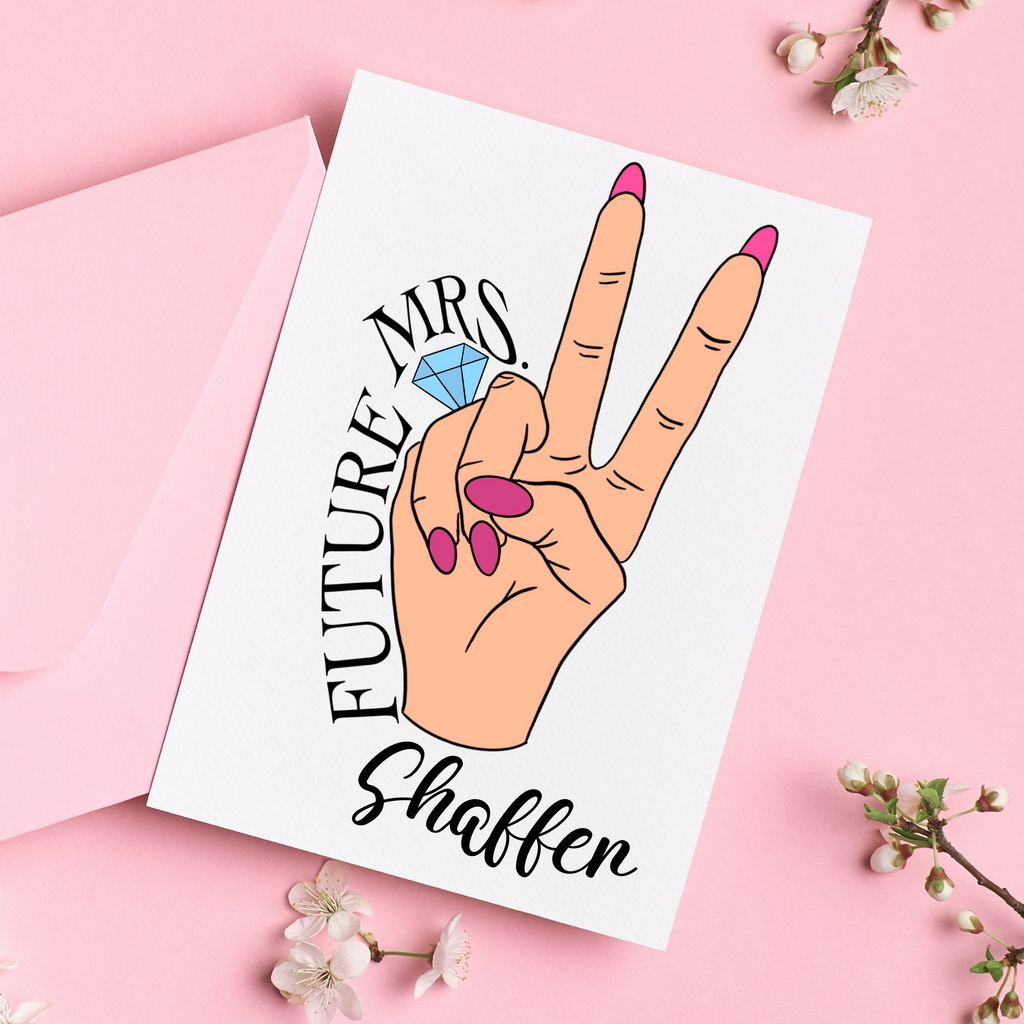 A personalized card, peace sign with a hand and pink nails with a ring on the fourth finger. Pink background and pink envelope with florals.Future Mrs Shaffer is written around the hand. A great personalized engagement gift for the newlywed.