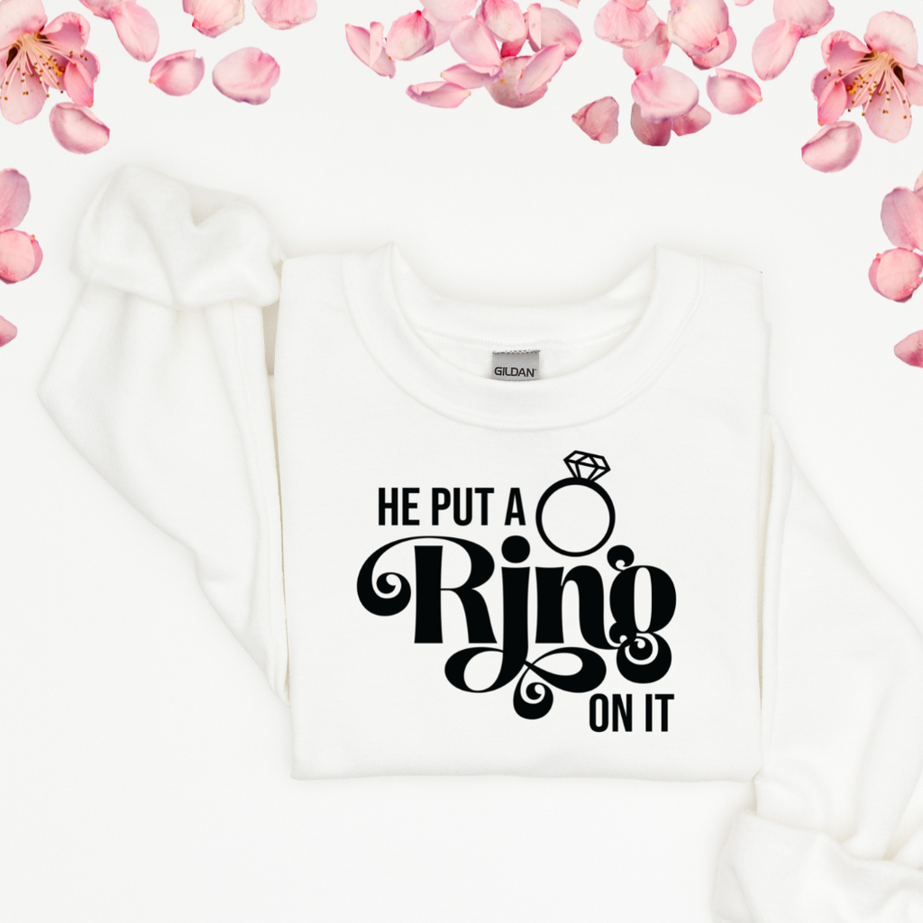 White crewneck laying flat with "he put a ring on it" written in black.