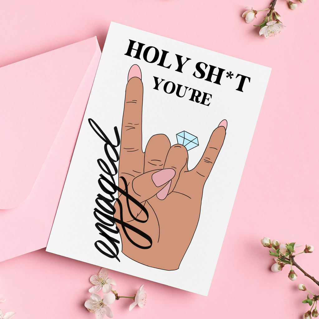 Holy Sh*T You're Engaged handmade card. Features a rock sign made with a hand with pink nails and a ring on the fourth finger. On a pink background with a pink envelope. A great bride-to-be card for the bridal shower from the funny bridesmaidsl