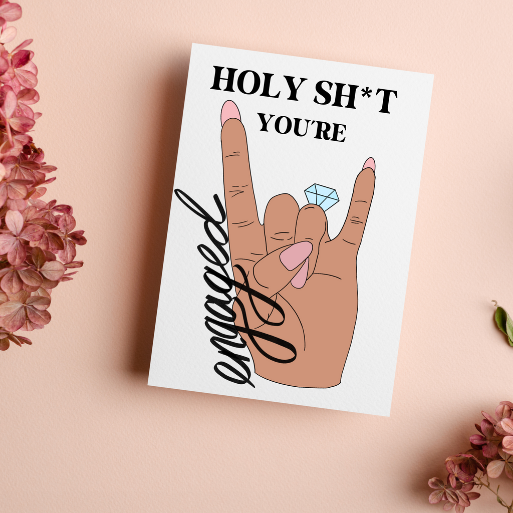 Holy Sh*T You're Engaged handmade card. Features a rock sign made with a hand with pink nails and a ring on the fourth finger. Sitting on a blush floral background. A funny engaging card for the newlywed. 