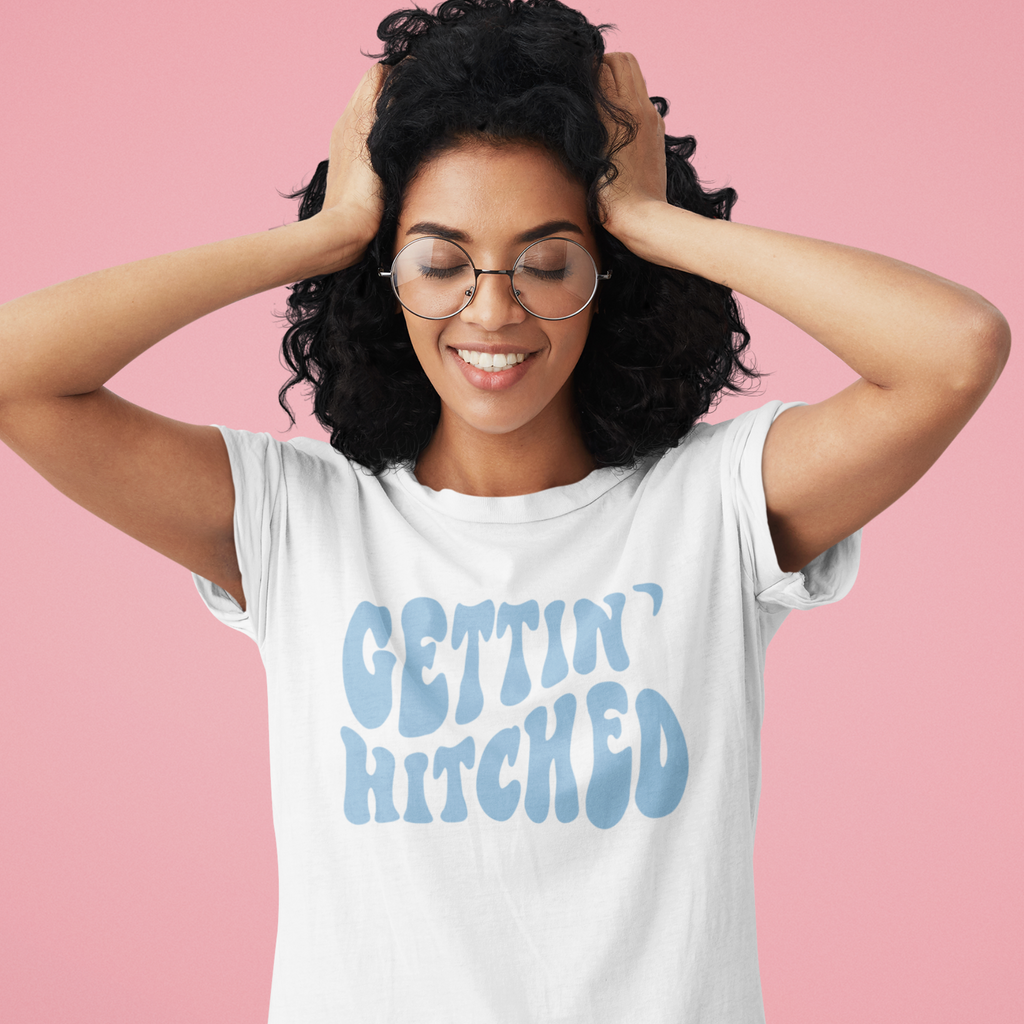 Young girl with hair in head wearing a white shirt with the words "Gettin' Hitched" in a light blue. Perfect gift for the bride to be.