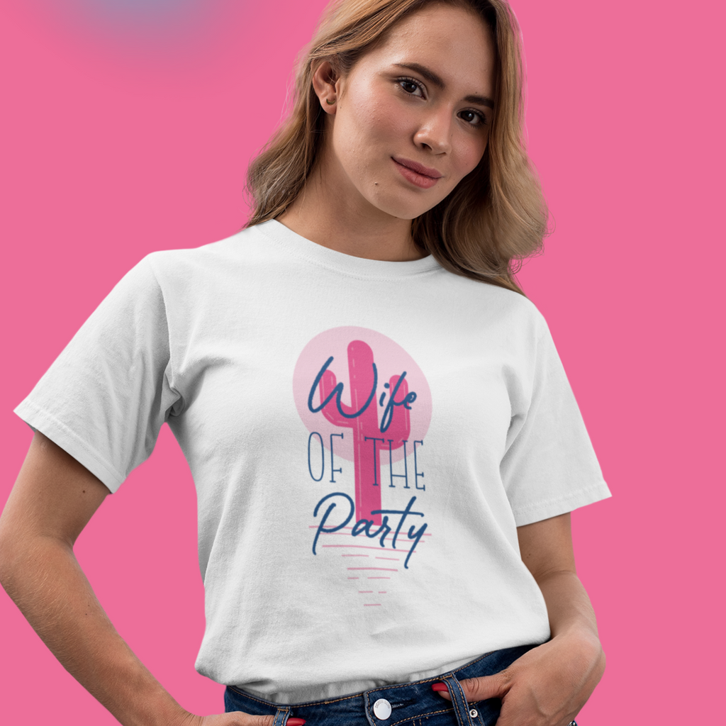 A young woman wearing a white shirt with the words "wife of the party" written overtop of a pink cactus. She is in front of a pink background and smiling. This is a great gift for a newlywed to lounge around in or wear on the bachelorette!