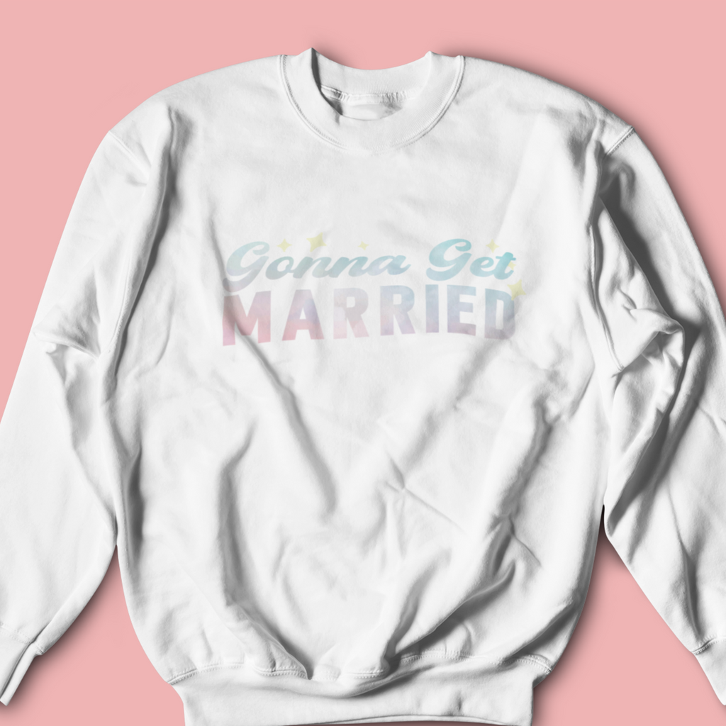 A white crewneck with "gonna get married" in pale blue/pink. On a blush background. A great gift for the newlywed as an engagement gift.
