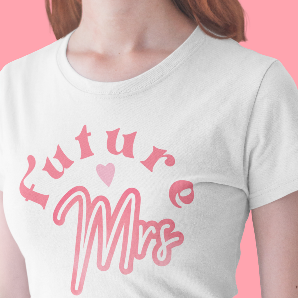 White T shirt with "Future <3 Mrs" written on the front. Worn by a woman on a pink background.