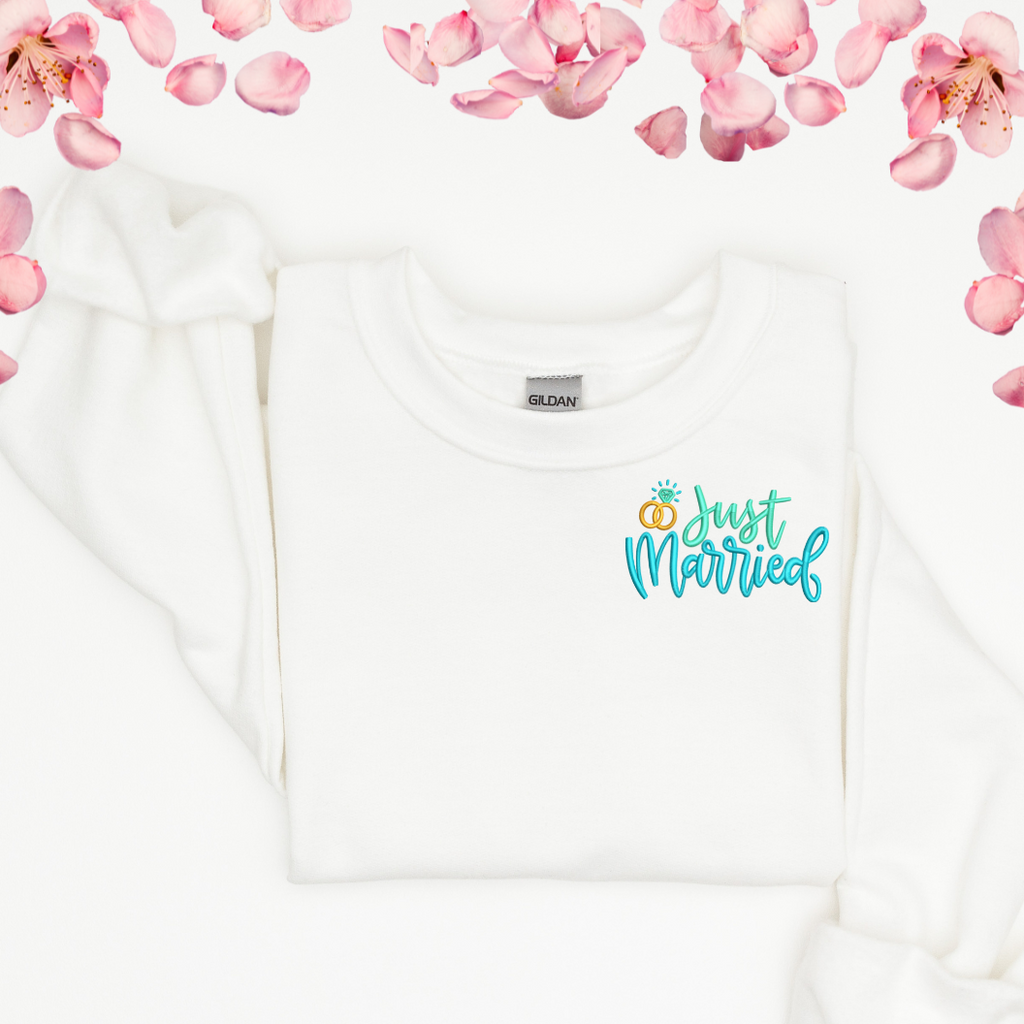 A white crewneck with "just married" embroidered in a turquoise color on the left hand side.