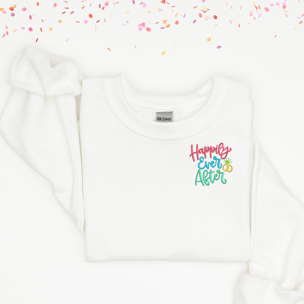 White crewneck with "happily ever after" embroidered in the left corner in pink, blue and green.