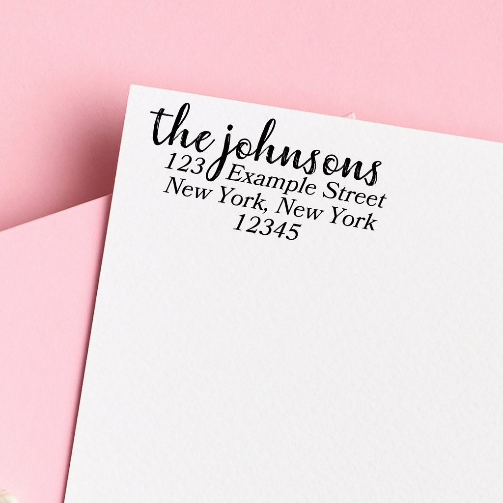 A stamp on an envelope - "the johnsons" written in calligraphy, "123 Example Street, New York New York, 12345" written in block letters below. On a pink background