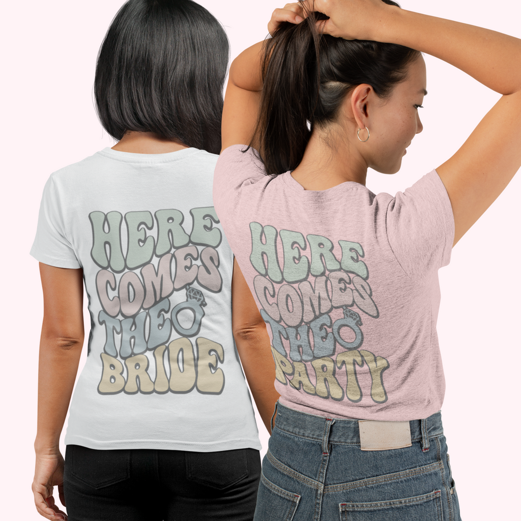 Two women showing the back of their t shirts - one is in white saying "here comes the bride" and the other is in pink wearing "here comes the party.