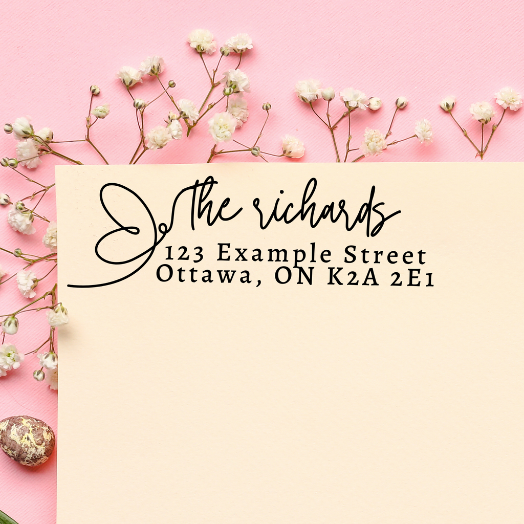 A black self inking stamp on a white nevelope. "The richards" written in cursive with a butterfly silhouette. The rest of the address is written in block writing. On a floral pink background. A great housewarming gift.