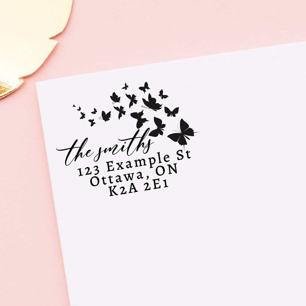 A black self inking stamp on a white envelope. Butterfly silhouettes surround the writing. "The smiths" written in calligraphy and the rest in block script. The envelope is on a floral pink background. A great newlywed gift.