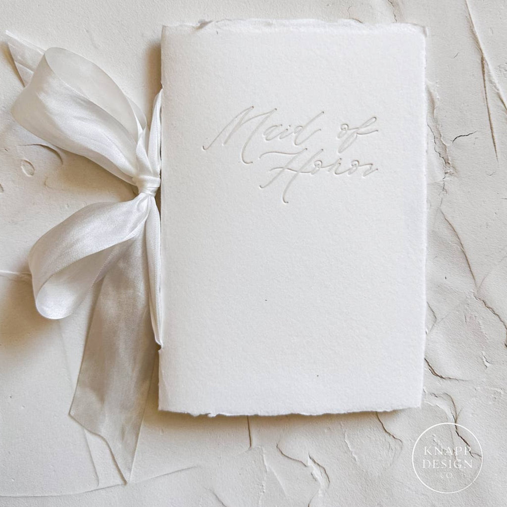 White vow book with silk ribbon and "maid of honor" pressed on the front