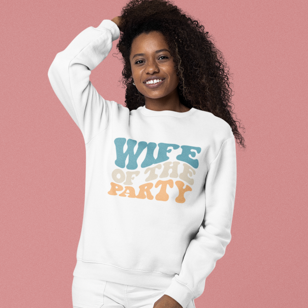 A young black woman wearing a white crewneck with "wife of the party" written in retro writing.