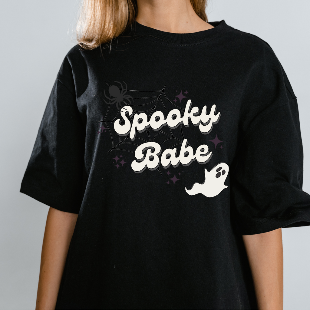 A woman wearing a black shirt with "spooky babe" printed on. Great for the halloween bachelorette!