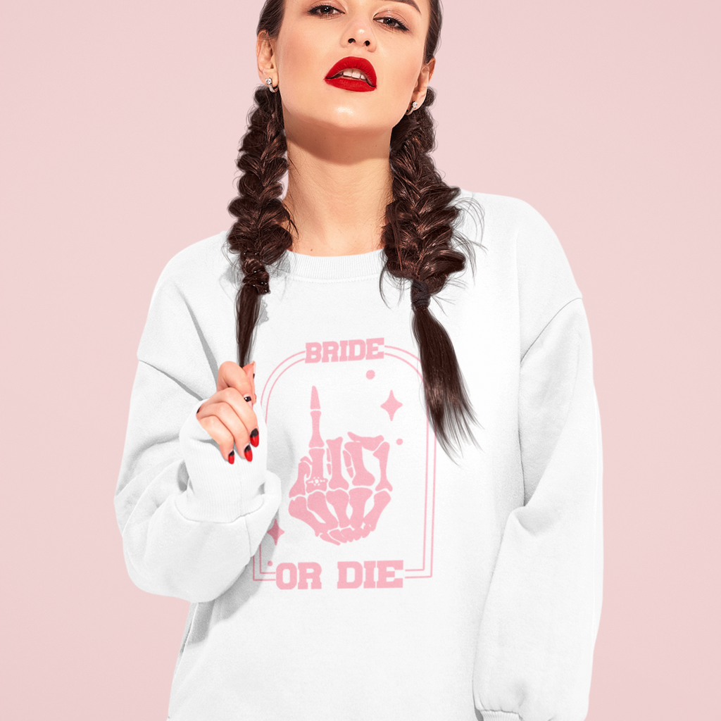 A young woman wearing a white sweatshirt printed with "bride or die" in pink on the front. A unique engagement gift.