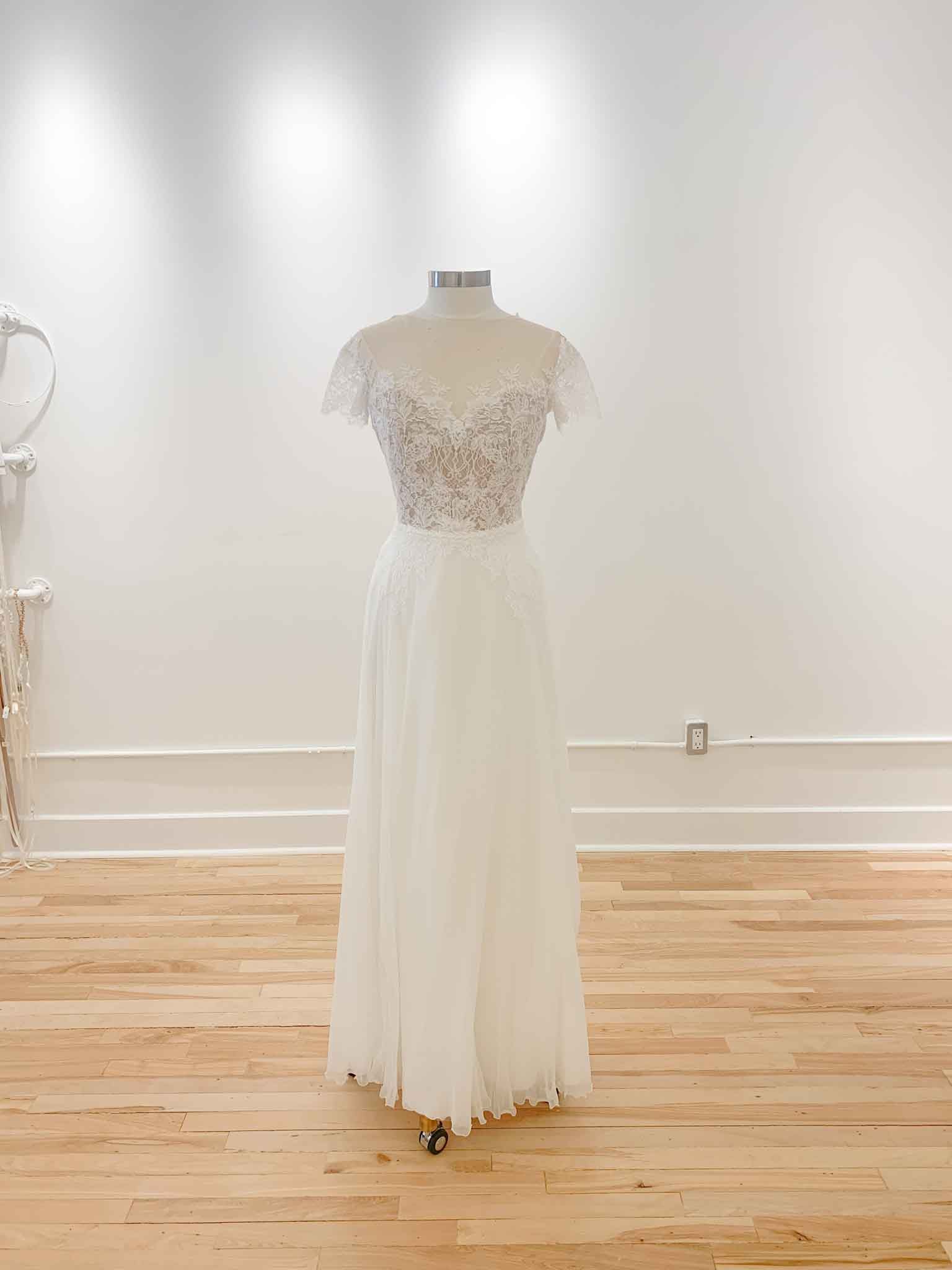 A backless, off-the shoulder, a-line gown with an illusion bodice, with added boning on a mannequin