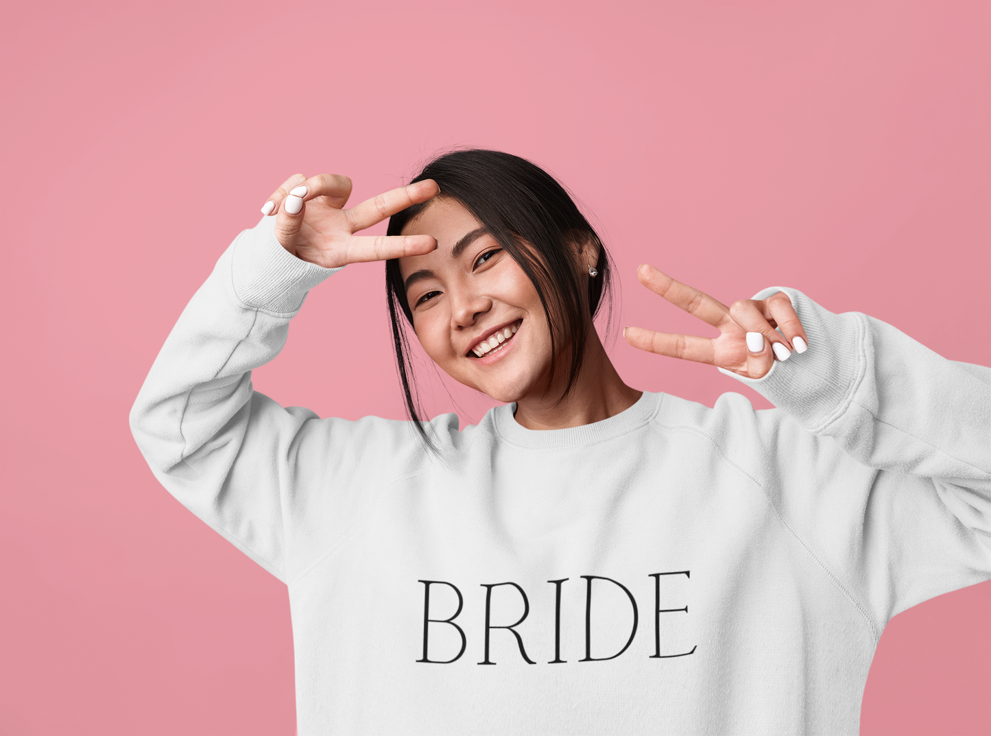 BRIDE written in black text on a white crewneck, worn by a young woman making a peace sign