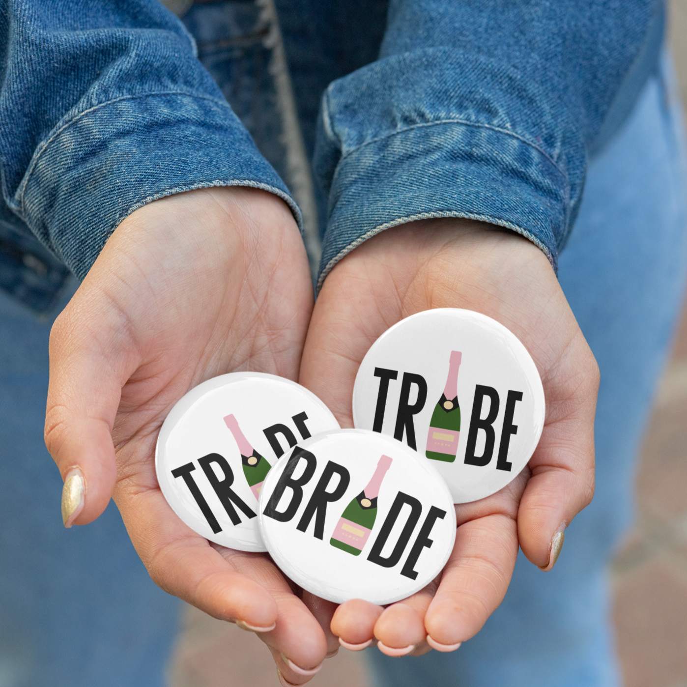 Hands holding white buttons with "bride" and "tribe", where the I is a champagne bottle